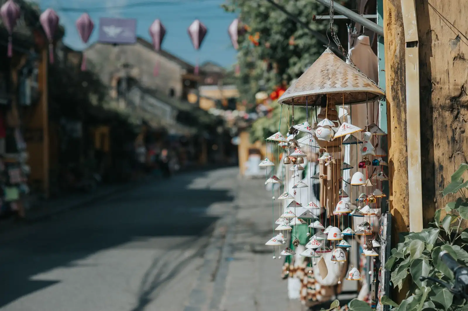 Conical hats and hanging lanterns adorn a quaint street in a traditional Asian town.