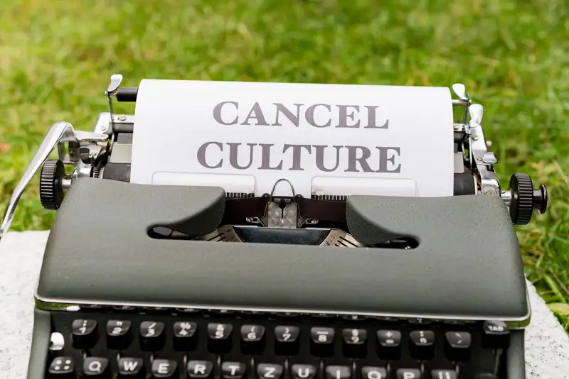 Retro typewriter with 'Cancel Culture' typed paper on grass background outdoors.